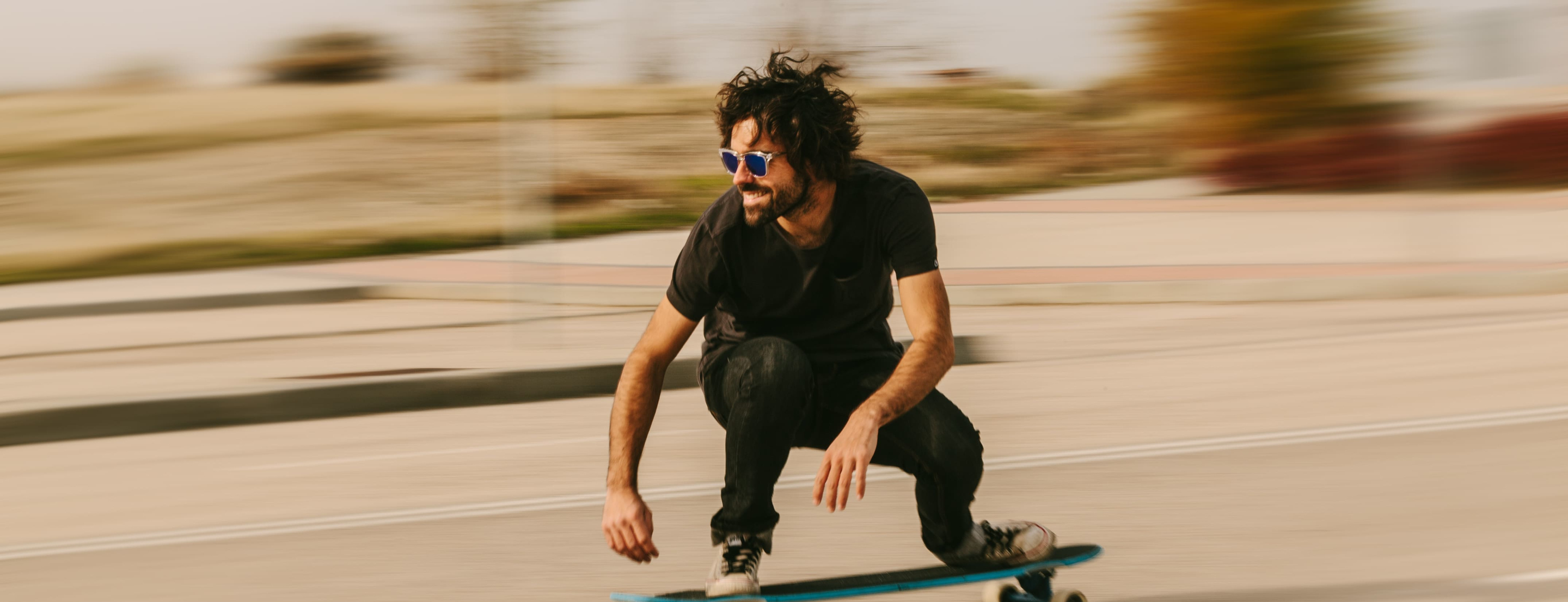 Skateur souriant, portant des lunettes bleues, en mouvement rapide sur la route.