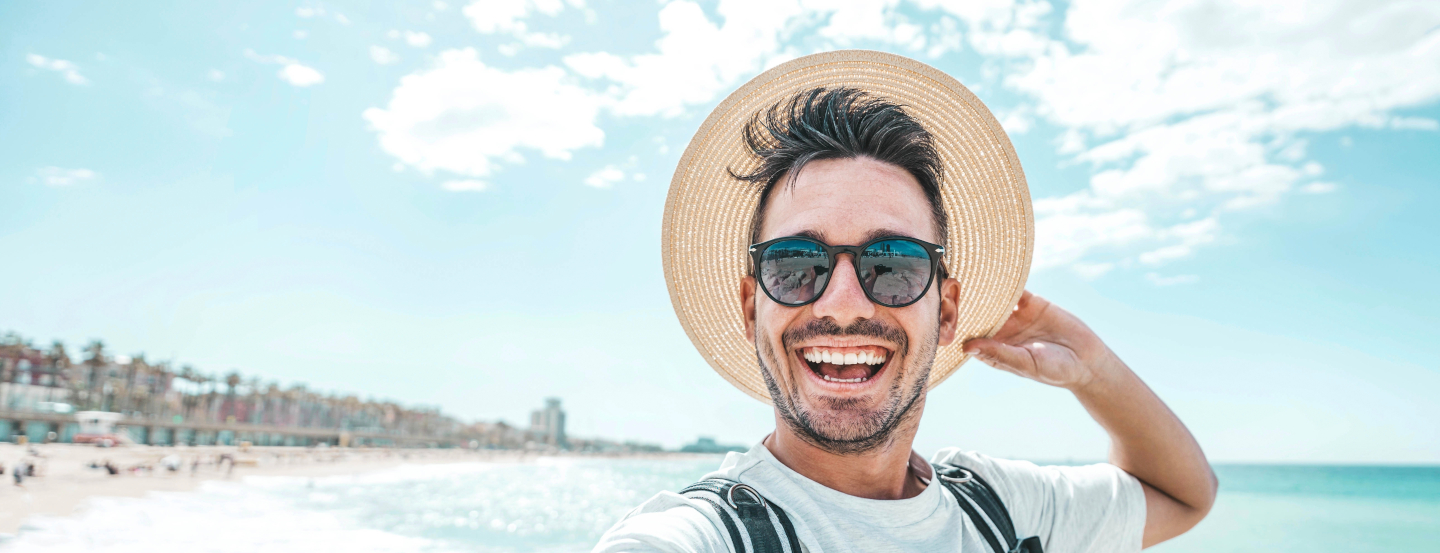 Homme portant un chapeau de paille, se tenant sur la plage avec la mer et le ciel en arrière-plan.
