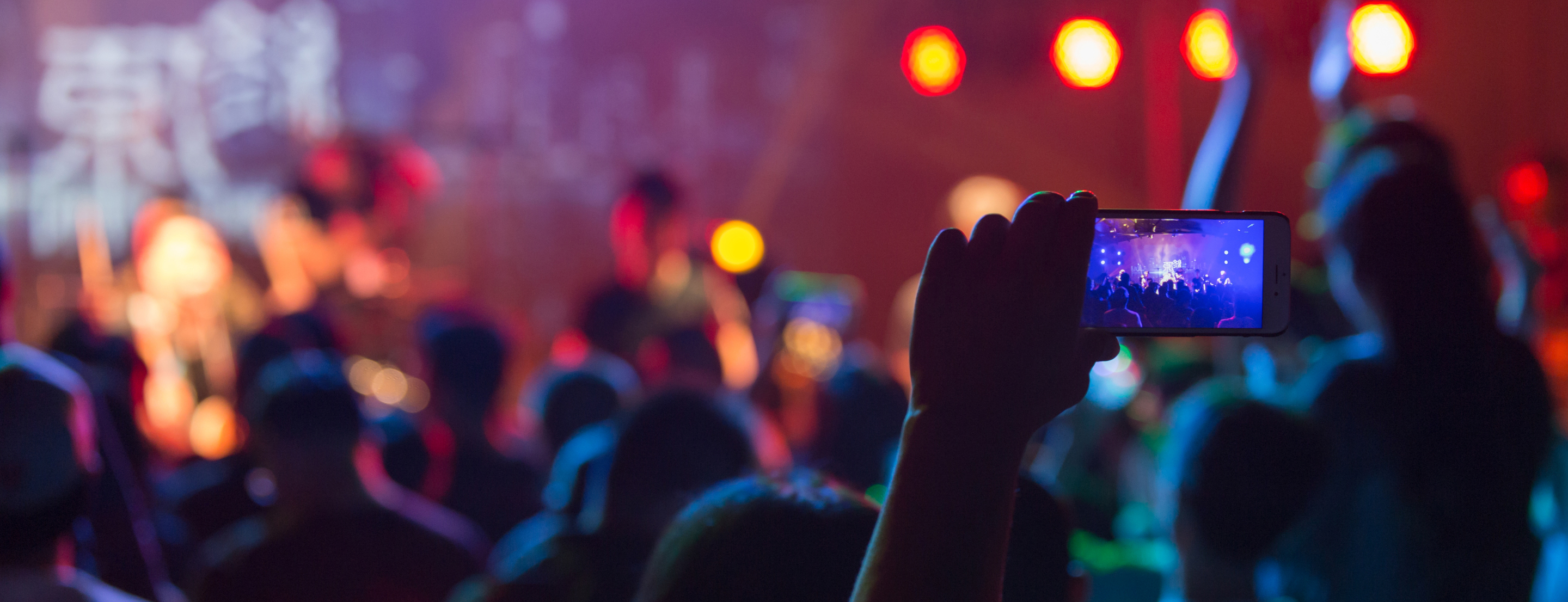 Une personne filme avec son téléphone un concert devant une foule éclairée de lumières colorées