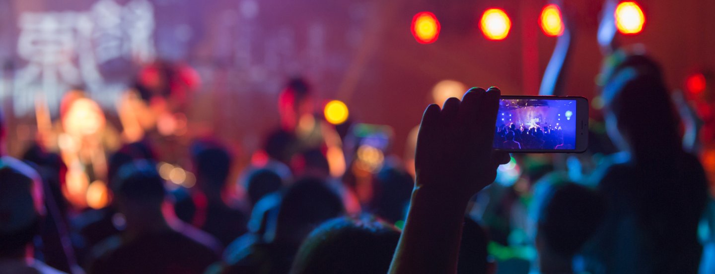 Une personne filme avec son téléphone un concert devant une foule éclairée de lumières colorées