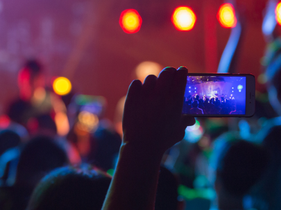 Une personne filme avec son téléphone un concert devant une foule éclairée de lumières colorées