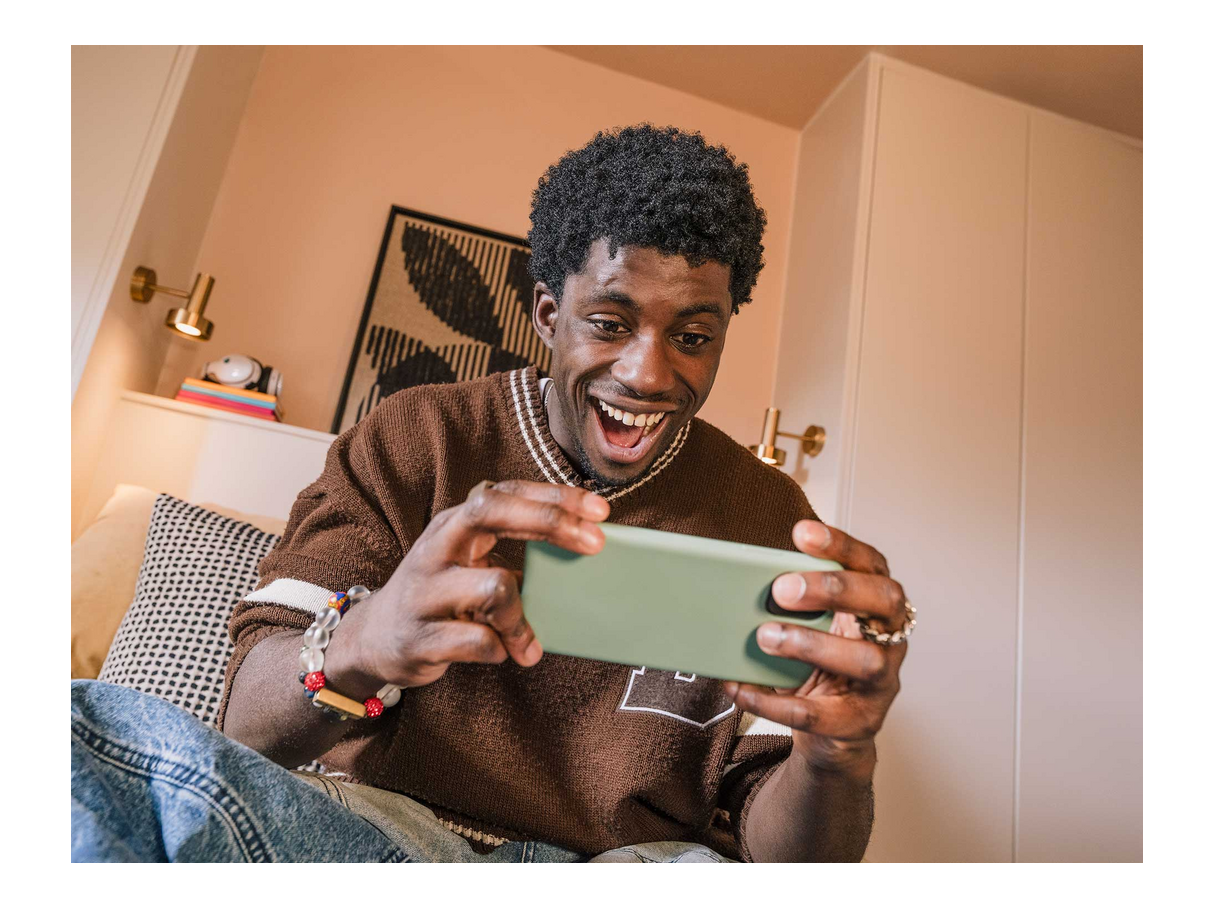 Homme souriant joue sur son téléphone dans un salon chaleureux.