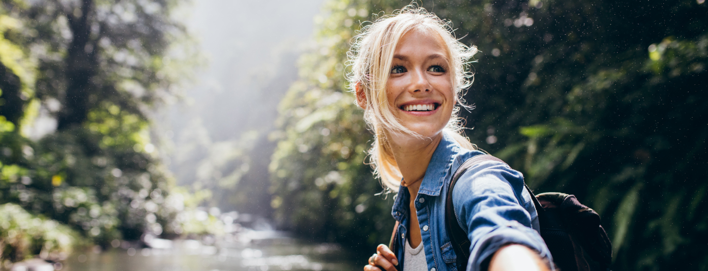 Personne prenant un selfie au bord d'une rivière, entourée de verdure et de lumière naturelle.