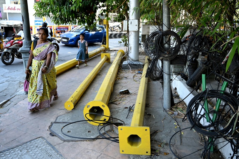 Une femme passe à côté de pylônes et de câbles sur un trottoir à Chennai, le 9 juillet 2026 en Inde