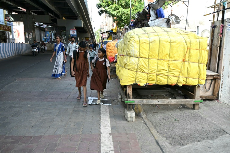Des écolières passent le long d'un trottoir bloqué par des marchandises entreposées dans une rue à Chennai, le 9 juillet 2026 en Inde