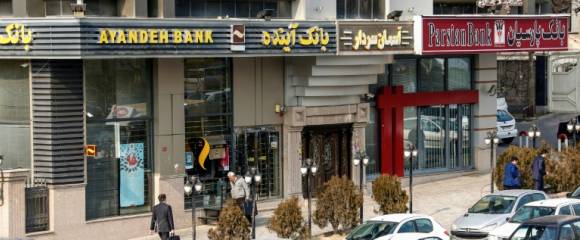Des Iraniens passent devant une succursale de la banque Ayandeh (G) dans la capitale Téhéran, le 14 janvier 2017 Des Iraniens passent devant une succursale de la banque Ayandeh (G) dans la capitale Téhéran, le 14 janvier 2017