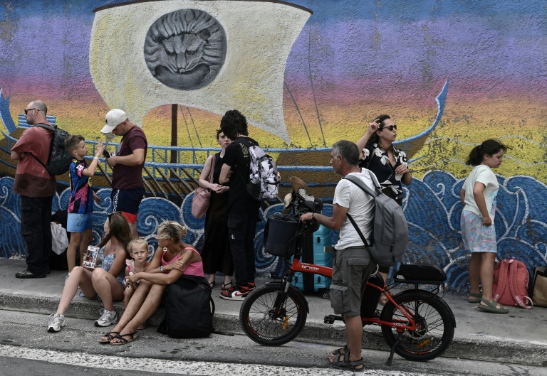 Des touristes turcs attendent dans une file d’attente devant le bureau des douanes, dans le village de Vathy, sur l’île de Samos, le 24 juillet 2026