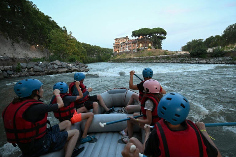 Des personnes naviguent en canot pneumatique sur le Tibre, passant devant l'île Tibérine, sur un tronçon du fleuve situé entièrement dans la zone urbaine du centre de Rome, le 14 août 2026.