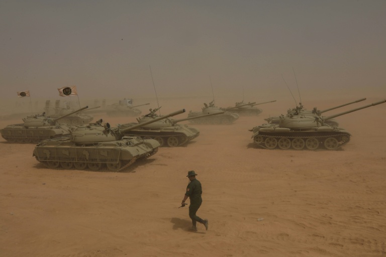Un soldat libyen marche devant des chars pendant des manoeuvres militaires de l'Armée nationale libyenne, le 16 mai 2026 dans le sud-est de la Libye