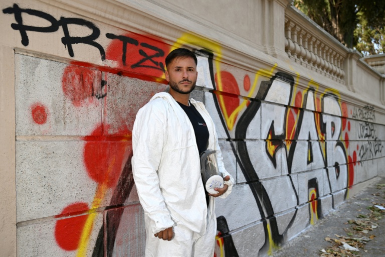 Valerio Tuveri, connu sur les réseaux comme "le gars qui nettoie Rome", pose avec en combinaison de protection avant de commencer à effacer un graffiti le long d'un mur de la Villa Sciarra, à Rome, le 27 juillet 2026