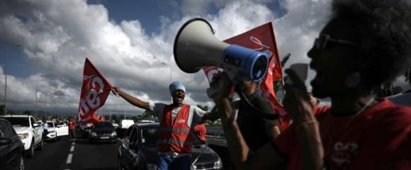 Des membres de la CGT Martinique manifestent le 15 octobre 2024 sur la route menant à l'aéroport de Fort-de-France, en plein mouvement contre la vie chère Des membres de la CGT Martinique manifestent le 15 octobre 2024 sur la route menant à l'aéroport de Fort-de-France, en plein mouvement contre la vie chère